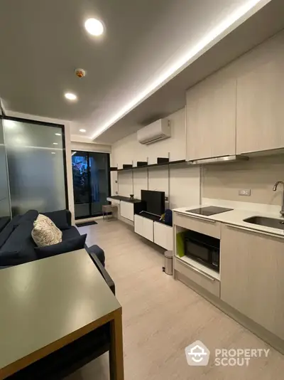 Modern studio apartment with integrated living space, featuring sleek kitchen with built-in oven, ample storage, and cozy sitting area.