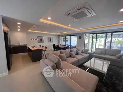 Spacious modern living room with open kitchen and large windows offering garden view.