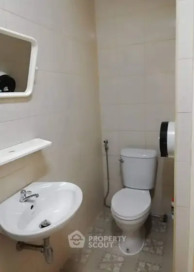 Compact bathroom with sink, toilet, and wall-mounted mirror in a tiled setting.