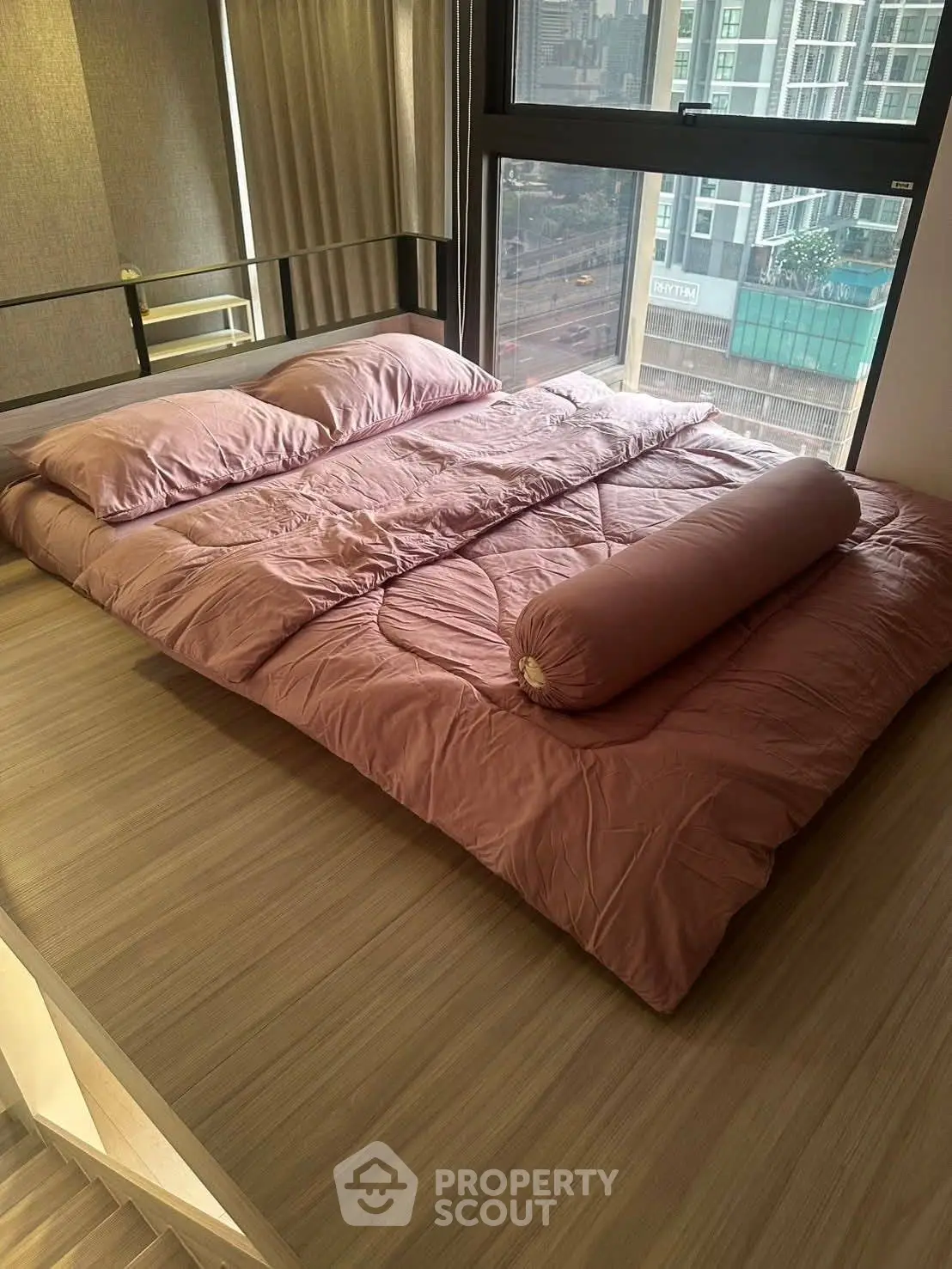 Modern bedroom with floor-to-ceiling windows and city view, featuring a cozy pink bedding set.