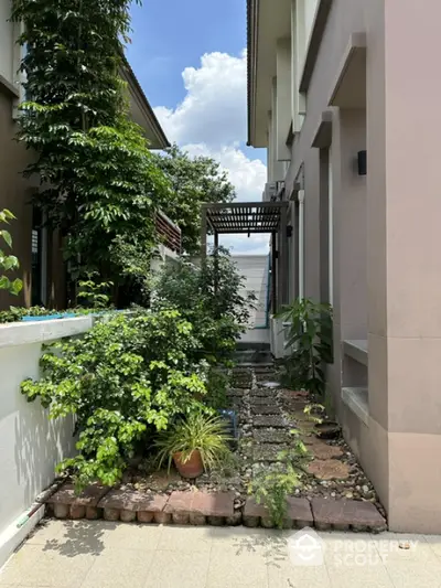 Charming garden pathway beside modern home with lush greenery and clear blue sky.