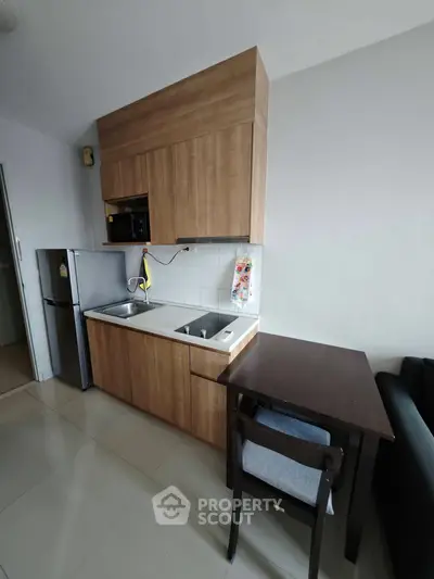 Modern compact kitchen with wooden cabinets and dining area in a cozy apartment.