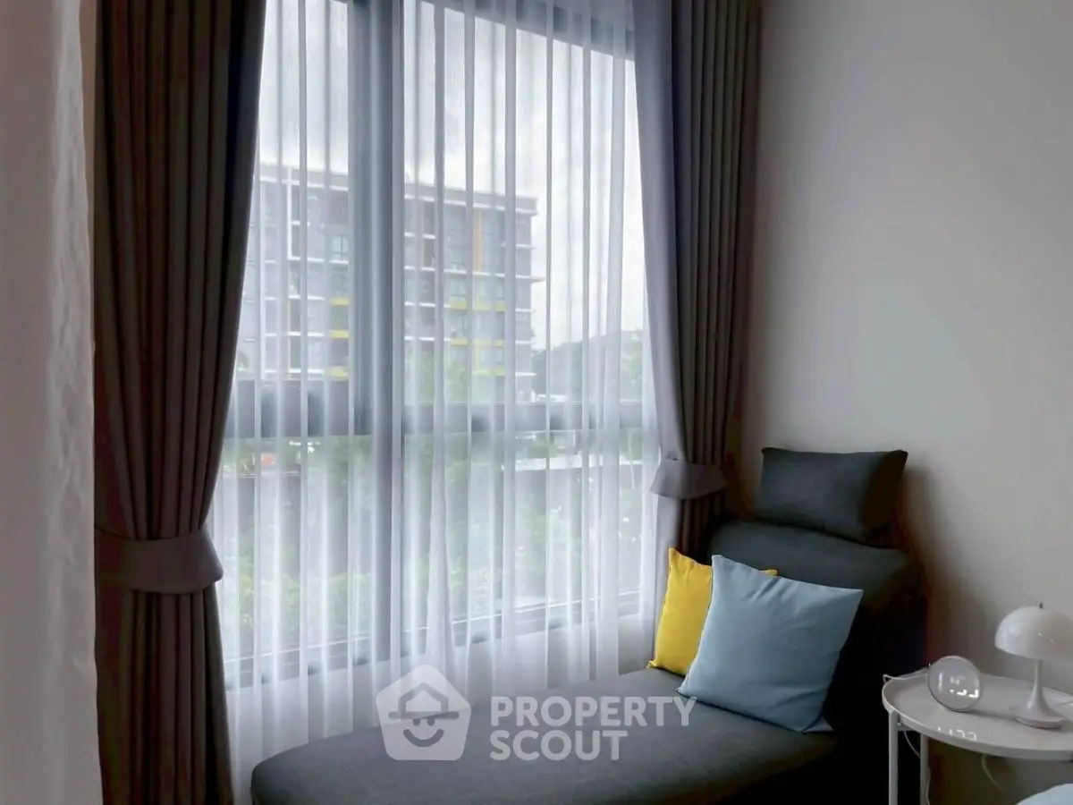 Cozy corner with modern chaise lounge and city view through large window.