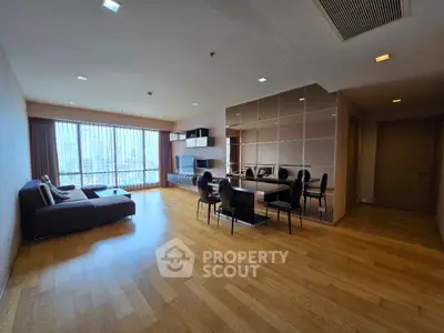 Spacious modern living room with wooden flooring and large windows offering city views.