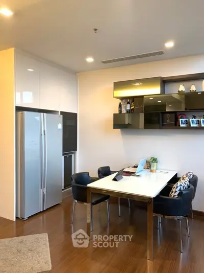 Modern kitchen with sleek dining area and stylish shelving, featuring a stainless steel fridge and elegant decor.