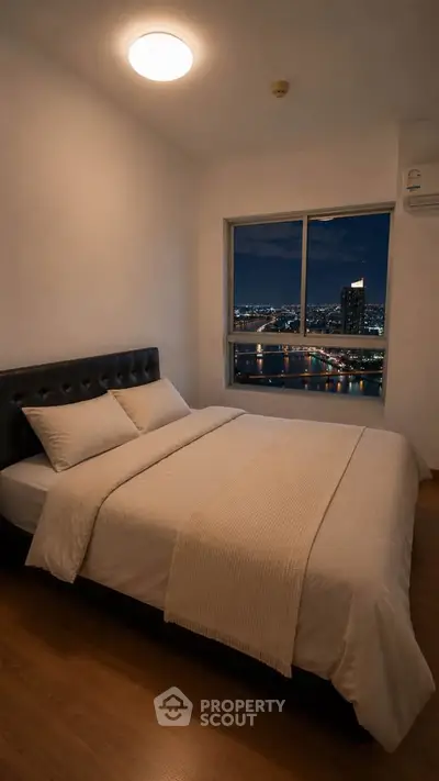 Cozy bedroom with city view, featuring a comfortable bed and large window overlooking the skyline.