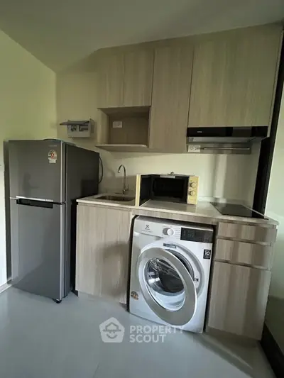 Modern compact kitchen with washing machine and microwave in sleek cabinetry.