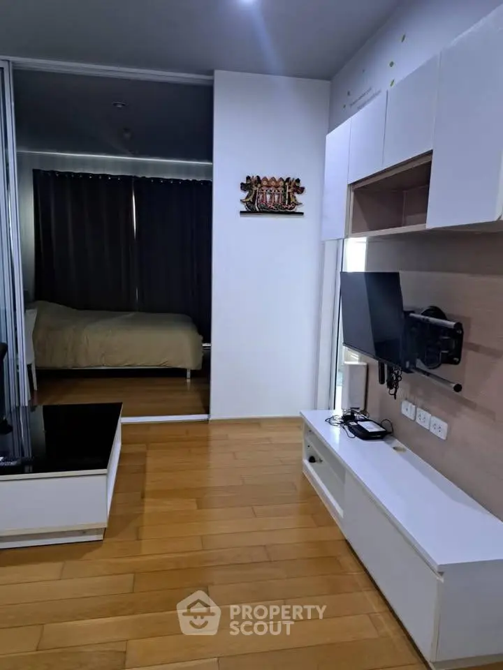Modern apartment interior with wooden flooring and wall-mounted TV, featuring a cozy bedroom in the background.