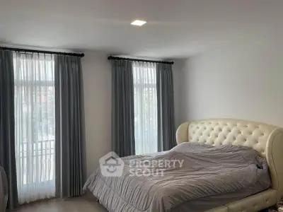 Spacious bedroom with elegant bed and large windows with sheer curtains.