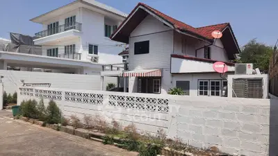 Charming two-story house with red roof and satellite dishes, surrounded by a white fence.