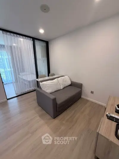 Modern living room with cozy gray sofa and wooden flooring, featuring a glass partition and sheer curtains.
