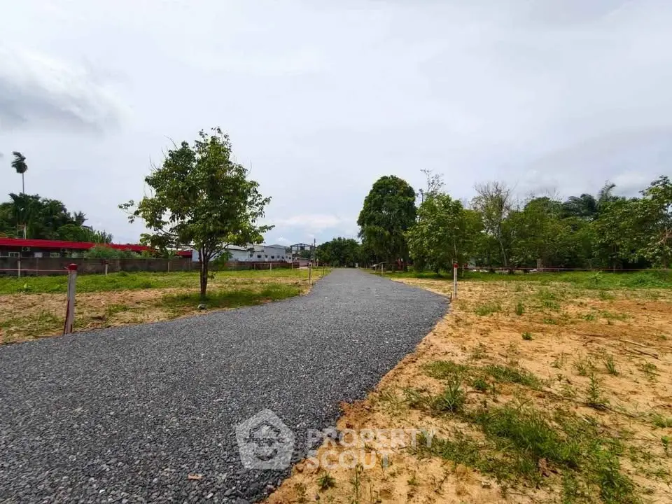Expansive plot of land with gravel path and lush greenery, perfect for development opportunities.