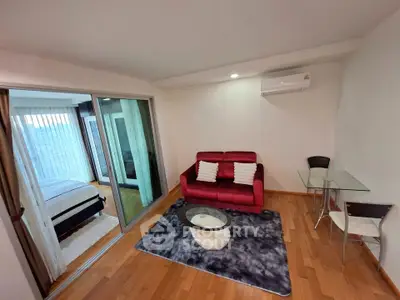 Modern living room with red sofa and glass table, adjacent to cozy bedroom