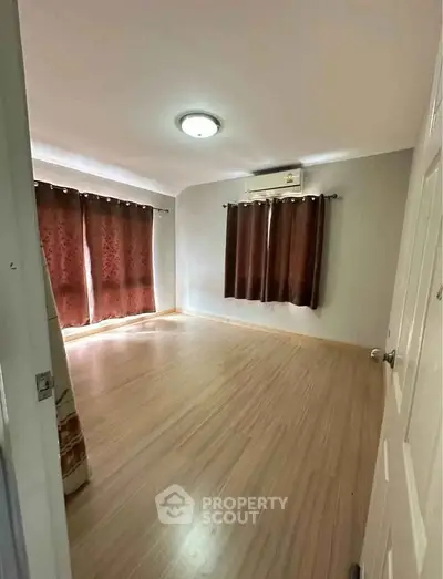 Spacious empty bedroom with wooden flooring and air conditioning, ready for customization.
