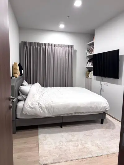Modern bedroom with cozy bed, wall-mounted TV, and elegant curtains.