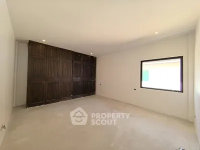 Spacious unfurnished room with large window and wooden accent wall, ideal for customization.