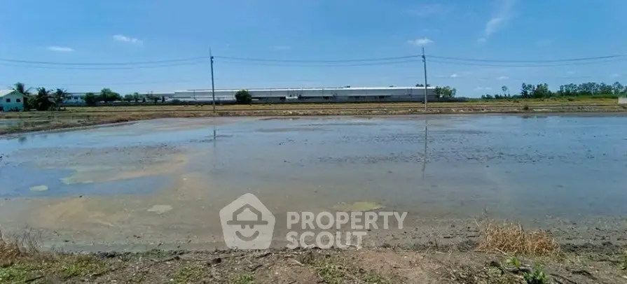 Expansive land with potential for development, featuring open fields and distant industrial building.