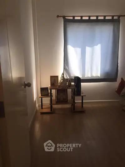 Cozy room with wooden flooring and a small shelf under a window with curtains.