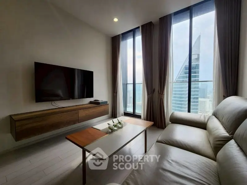Modern living room with large windows and city view, featuring sleek furniture and a wall-mounted TV.