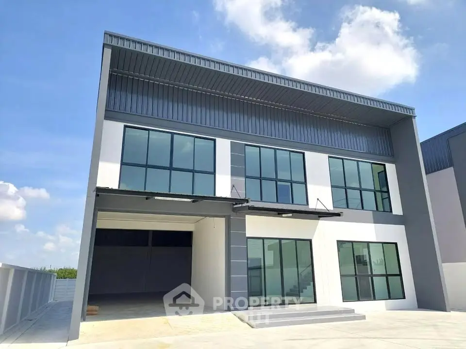 Modern industrial building with large glass windows and spacious garage under a clear blue sky.
