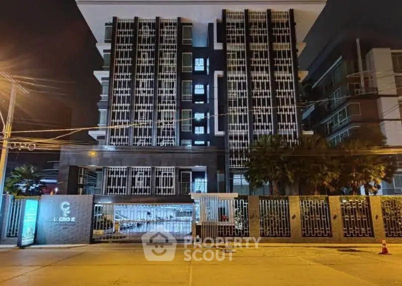 Modern apartment building exterior with unique architectural design and gated entrance at night.