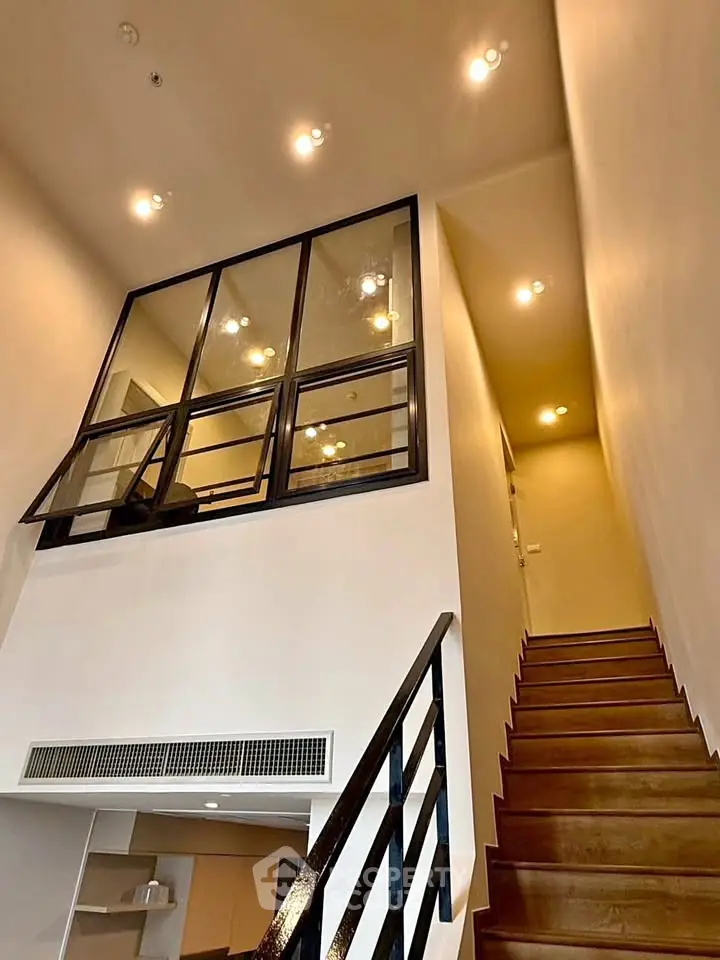 Modern duplex interior with stylish staircase and glass partition, showcasing high ceilings and elegant lighting.