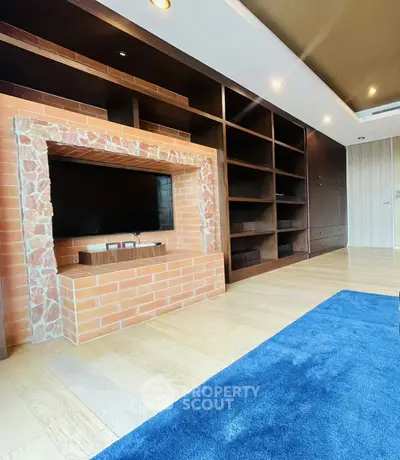 Spacious living room with built-in shelves and brick fireplace, featuring modern wooden flooring and blue rug.