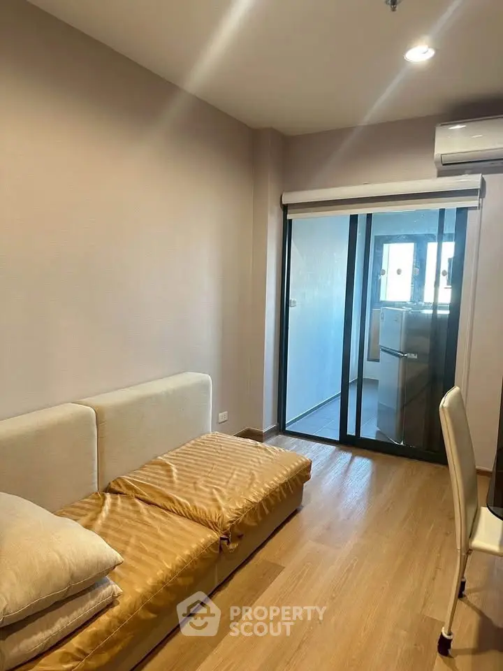 Cozy living room with sliding glass doors leading to a balcony, featuring a compact sofa and air conditioning.