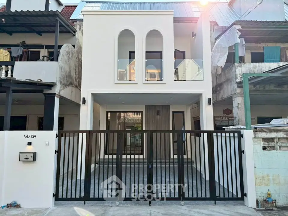 Modern two-story house with gated entrance and balcony, showcasing contemporary architecture and clean lines.