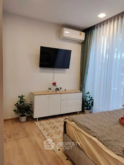 Modern bedroom with stylish decor, wall-mounted TV, and natural light from large windows.