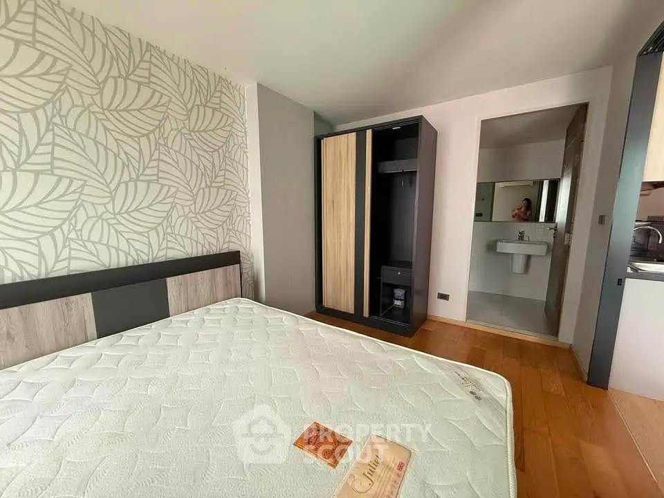Cozy bedroom with modern wardrobe and ensuite bathroom, featuring stylish leaf-patterned wallpaper.