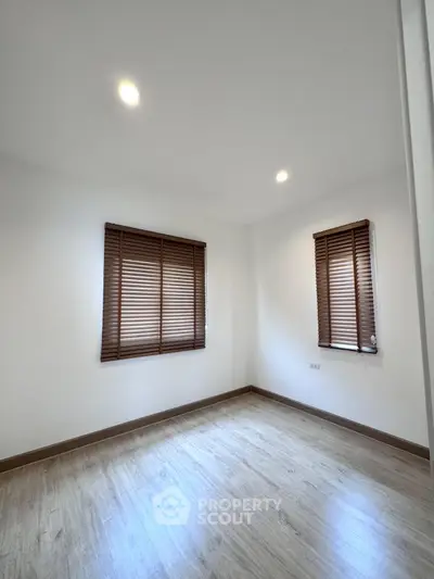 Spacious empty room with wooden flooring and window blinds, perfect for customization.