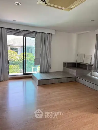 Spacious living room with large windows and wooden flooring, offering a serene view of greenery.
