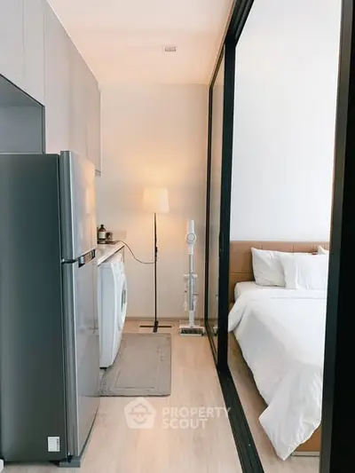 Modern studio apartment with sleek kitchen and cozy bedroom separated by glass partition.