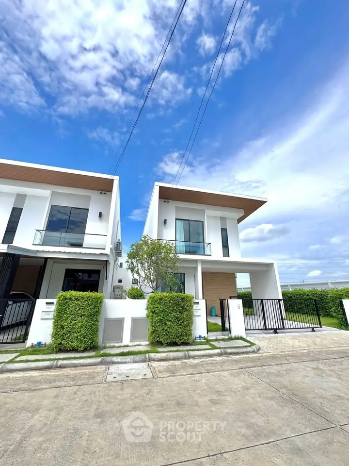 Modern two-story white houses with sleek design and lush greenery under a clear blue sky.