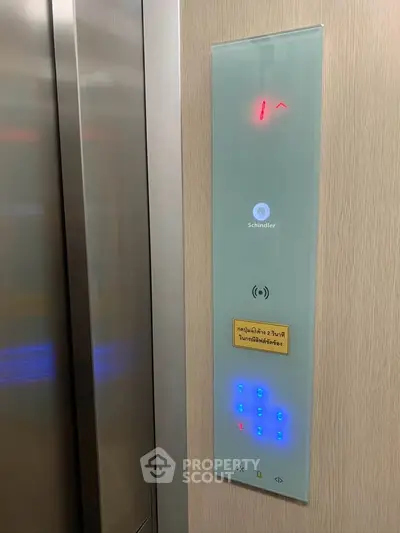 Modern elevator control panel with digital display and touch buttons in a sleek building.