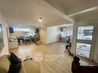 Spacious open-plan living room with modern kitchen and exercise area, featuring large windows and wooden flooring.
