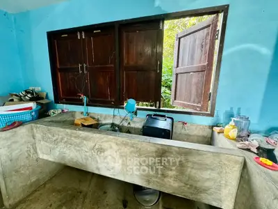 Rustic kitchen with concrete sink and wooden windows, offering a natural view.