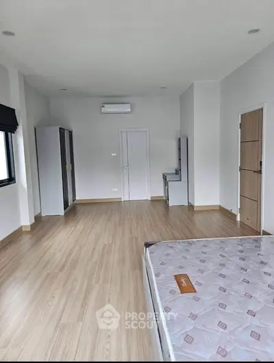 Spacious bedroom with modern design and wooden flooring, featuring a large window and air conditioning.