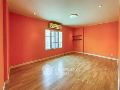 Spacious empty room with vibrant orange walls and wooden flooring, ideal for customization.