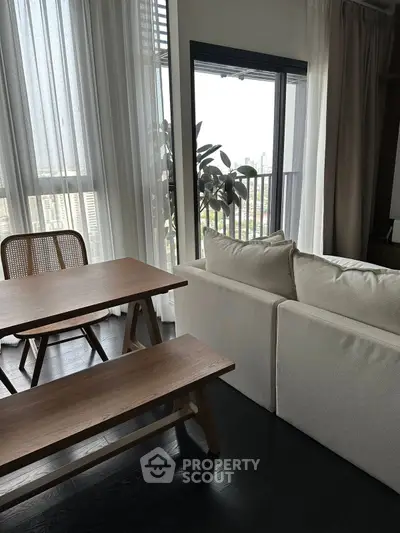 Modern living room with cozy sofa and dining table, featuring large windows with city view.