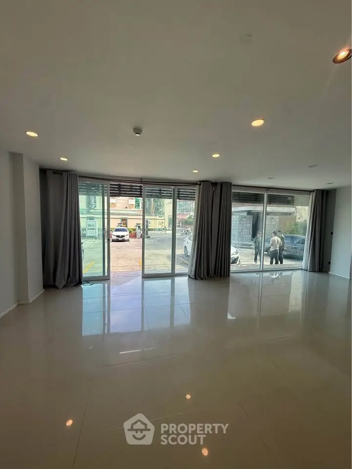 Spacious living room with large windows and modern tile flooring, offering ample natural light and outdoor view.