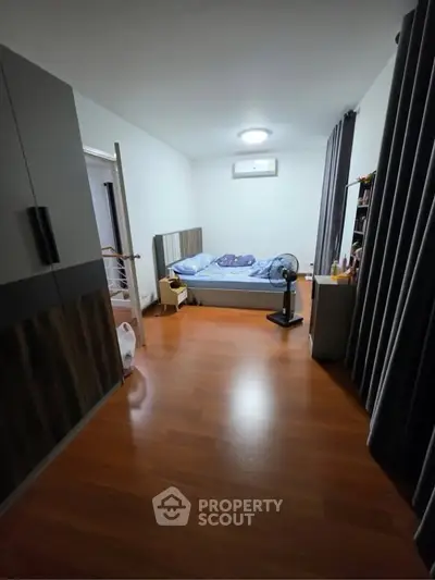 Spacious bedroom with wooden flooring and modern furnishings in a cozy apartment.