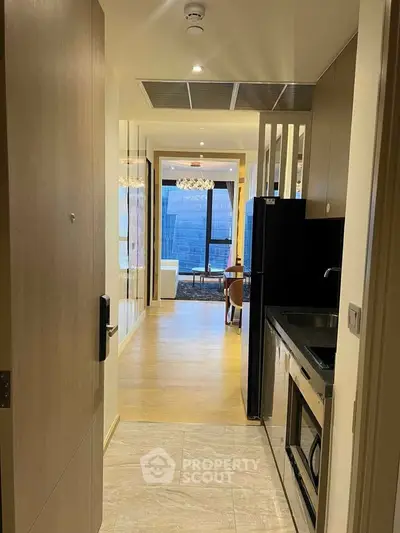 Modern apartment entrance with sleek kitchen and open living area, featuring stylish lighting and city view.