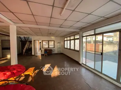 Spacious living room with large windows and natural light, featuring a staircase and tiled flooring.