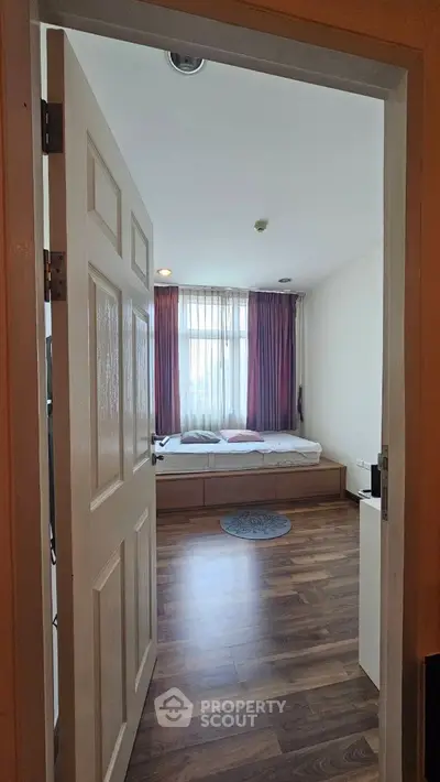 Cozy bedroom with wooden flooring and large window for natural light