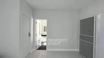 Minimalist interior with white walls and tiled floor, leading to a bathroom with a modern sink.