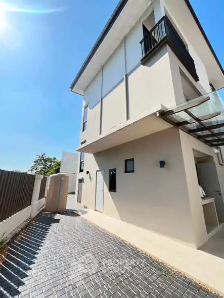 Modern three-story building with sleek design and spacious driveway under clear blue sky.
