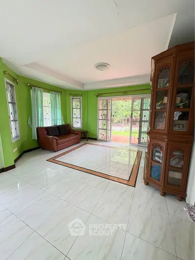 Spacious living room with green walls, large windows, and elegant wooden cabinet.