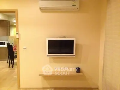 Modern living room with wall-mounted TV and air conditioning unit, open kitchen view.
